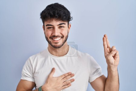 Téléchargez les photos : Homme hispanique avec la barbe debout sur fond blanc en jurant souriant avec la main sur la poitrine et les doigts vers le haut, faisant un serment de fidélité - en image libre de droit