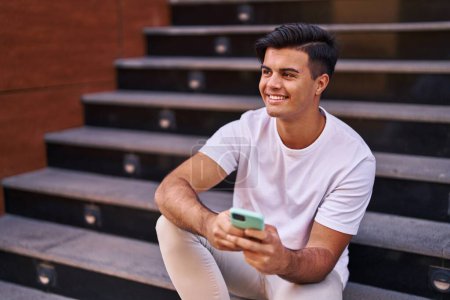 Photo for Young hispanic man using smartphone sitting on stairs at street - Royalty Free Image