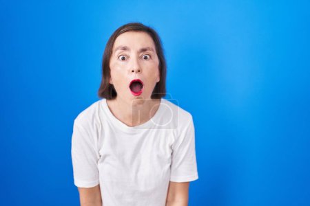 Photo for Middle age hispanic woman standing over blue background afraid and shocked with surprise and amazed expression, fear and excited face. - Royalty Free Image