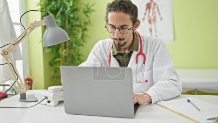 Téléchargez les photos : Young hispanic man doctor using laptop working at clinic - en image libre de droit