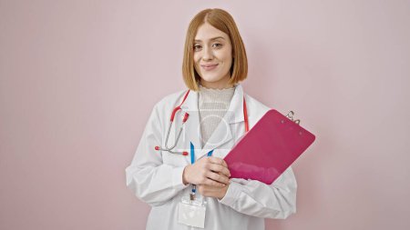 Téléchargez les photos : Jeune femme blonde médecin souriant confiant tenant presse-papiers sur fond rose isolé - en image libre de droit