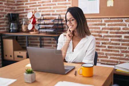 Photo for Hispanic young woman working at the office wearing glasses smiling looking confident at the camera with crossed arms and hand on chin. thinking positive. - Royalty Free Image
