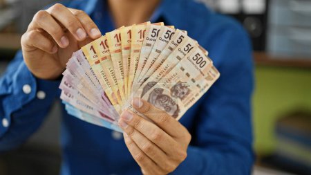 Foto de Joven trabajador de negocios hispano sostiene billetes mexicanos en la oficina - Imagen libre de derechos