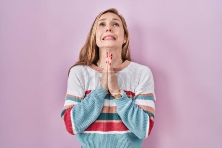 Photo for Young blonde woman standing over pink background begging and praying with hands together with hope expression on face very emotional and worried. begging. - Royalty Free Image