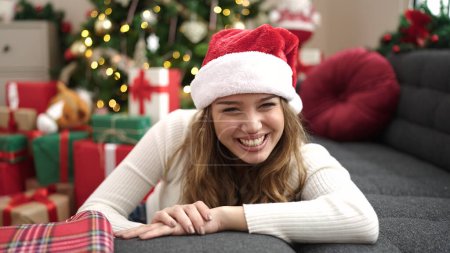 Foto de Joven mujer hispana hermosa sonriendo confiada sentada en el suelo por el árbol de Navidad en casa - Imagen libre de derechos