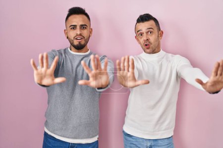 Téléchargez les photos : Couple homosexuel debout sur fond rose faisant geste d'arrêt avec les mains paumes de main, expression de colère et de frustration - en image libre de droit