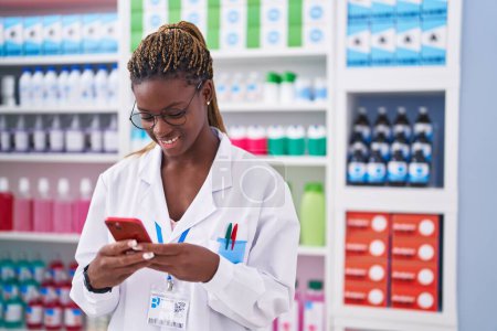 Photo for African american woman pharmacist using smartphone working at pharmacy - Royalty Free Image