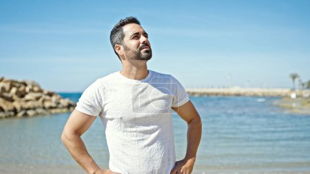 Téléchargez les photos : Jeune homme hispanique regardant vers le côté avec une expression sérieuse à la plage - en image libre de droit