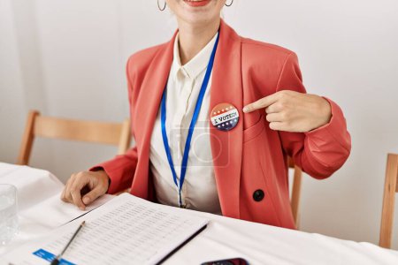 Foto de Joven mujer rubia presidente de la mesa electoral señalando que voté placa en el colegio electoral - Imagen libre de derechos