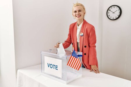Foto de Joven mujer rubia presidente de mesa electoral poniendo votación en urnas en colegio electoral - Imagen libre de derechos