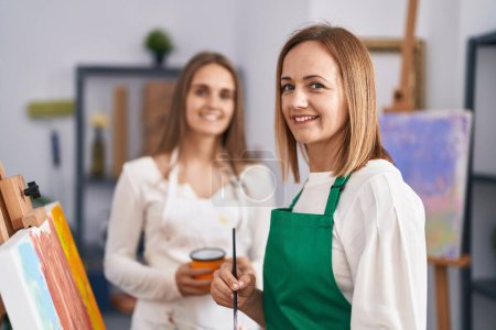 Photo for Two women artists smiling confident drinking coffee drawing at art studio - Royalty Free Image