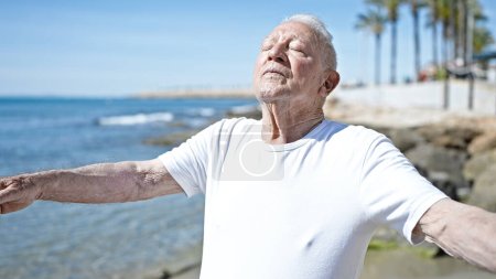 Foto de Hombre de pelo gris mayor respirando con los ojos cerrados a orillas del mar - Imagen libre de derechos