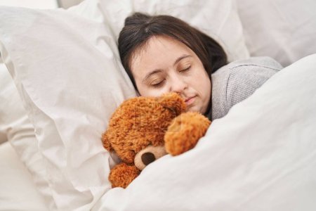 Téléchargez les photos : Jeune femme atteinte du syndrome du duvet couchée sur le lit dormant avec un ours en peluche dans la chambre - en image libre de droit