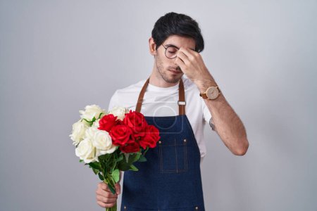 Téléchargez les photos : Jeune homme hispanique tenant un bouquet de roses blanches et rouges fatigué se frottant le nez et les yeux ressentant fatigue et maux de tête. concept de stress et de frustration. - en image libre de droit