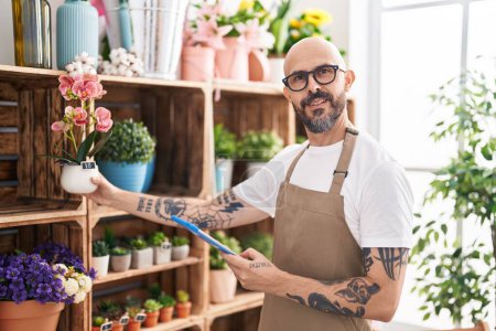 Photo for Young bald man florist using touchpad holding plant at florist - Royalty Free Image