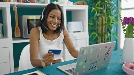 Photo for African american woman having video call holding credit card at dinning room - Royalty Free Image