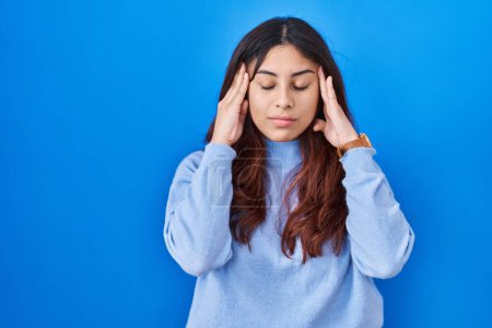 Photo for Hispanic young woman standing over blue background with hand on head, headache because stress. suffering migraine. - Royalty Free Image