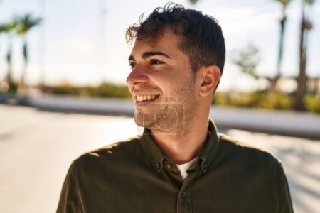 Foto de Joven hombre hispano sonriendo confiado mirando a un lado en el parque - Imagen libre de derechos