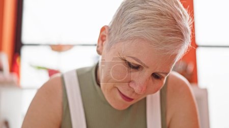 Photo for Middle age grey-haired woman looking down with serious expression at dinning room - Royalty Free Image