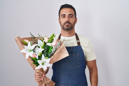 Téléchargez les photos : Homme hispanique avec barbe travaillant comme fleuriste détendue avec une expression sérieuse sur le visage. simple et naturel regardant la caméra. - en image libre de droit