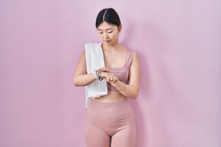 Photo for Chinese young woman wearing sportswear and towel checking the time on wrist watch, relaxed and confident - Royalty Free Image