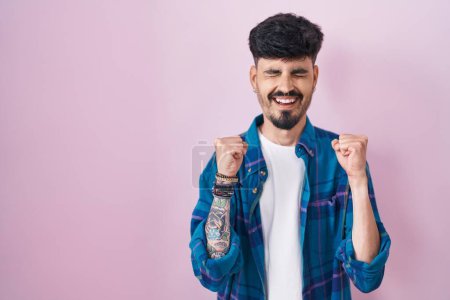 Photo for Young hispanic man with beard standing over pink background excited for success with arms raised and eyes closed celebrating victory smiling. winner concept. - Royalty Free Image