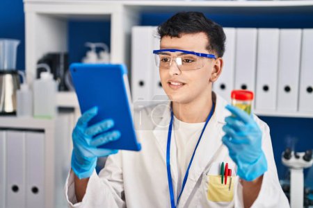 Foto de Joven hombre científico no binario sosteniendo tubo de prueba de orina usando touchpad en el laboratorio - Imagen libre de derechos