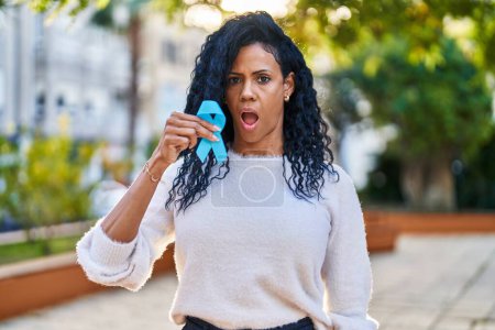 Téléchargez les photos : Moyen Age femme hispanique tenant ruban bleu effrayé et étonné avec la bouche ouverte pour la surprise, visage incrédule - en image libre de droit