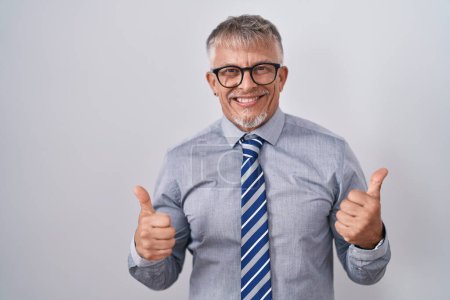 Téléchargez les photos : Homme d'affaires hispanique aux cheveux gris portant des lunettes signe de réussite faire un geste positif avec la main, pouces levés souriant et heureux. expression joyeuse et geste gagnant. - en image libre de droit