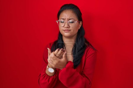 Téléchargez les photos : Asiatique jeune femme debout sur fond rouge souffrant de douleur aux mains et aux doigts, inflammation de l'arthrite - en image libre de droit