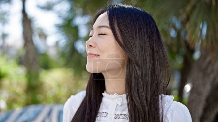 Photo for Young chinese woman breathing with closed eyes at park - Royalty Free Image