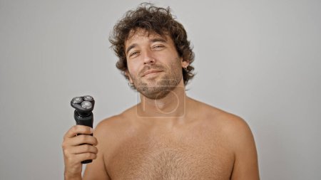 Foto de Joven hombre hispano masajeando oso sosteniendo máquina de afeitar sonriendo sin camisa sobre fondo blanco aislado - Imagen libre de derechos