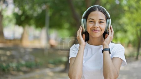Foto de Mujer afroamericana sonriendo confiada escuchando música en el parque - Imagen libre de derechos