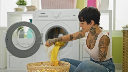 Photo for Hispanic woman with amputee arm washing clothes sitting on floor at laundry room - Royalty Free Image