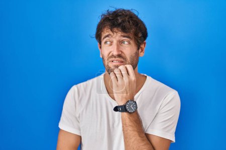 Photo for Hispanic young man standing over blue background looking stressed and nervous with hands on mouth biting nails. anxiety problem. - Royalty Free Image