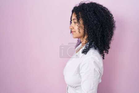 Photo for Hispanic woman with curly hair standing over pink background looking to side, relax profile pose with natural face and confident smile. - Royalty Free Image