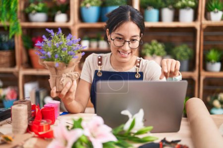 Téléchargez les photos : Jeune femme hispanique travaillant au magasin de fleuriste faire appel vidéo pointant vers vous et la caméra avec les doigts, souriant positif et joyeux - en image libre de droit