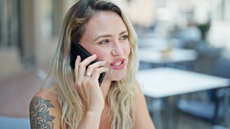 Téléchargez les photos : Jeune femme blonde parlant sur le smartphone assis sur la table à la terrasse du café - en image libre de droit
