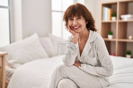 Téléchargez les photos : Femme d'âge moyen souriant confiant assis sur le lit dans la chambre - en image libre de droit