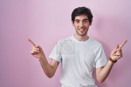 Foto de Young hispanic man standing over pink background smiling confident pointing with fingers to different directions. copy space for advertisement - Imagen libre de derechos