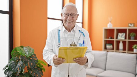 Téléchargez les photos : Homme âgé aux cheveux gris médecin lisant le document sur presse-papiers à la clinique - en image libre de droit