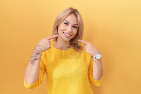 Téléchargez les photos : Jeune femme caucasienne portant un pull jaune souriant et joyeux montrant et pointant du doigt les dents et la bouche. concept de santé dentaire. - en image libre de droit