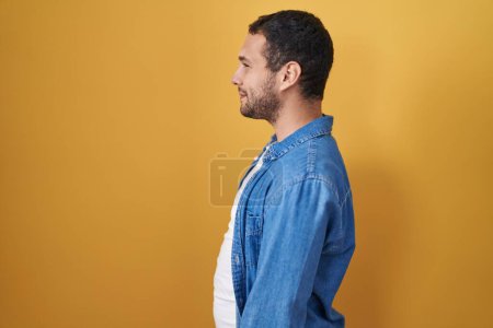 Téléchargez les photos : Homme hispanique debout sur fond jaune regardant vers le côté, pose de profil relax avec visage naturel et sourire confiant. - en image libre de droit