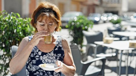 Téléchargez les photos : Femme d'âge moyen buvant du café assis sur la table à café terrasse - en image libre de droit