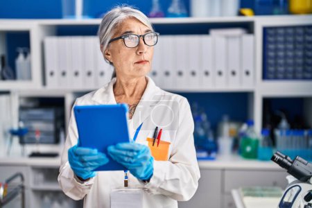 Photo for Middle age grey-haired woman scientist using touchpad working at laboratory - Royalty Free Image