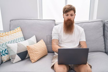 Téléchargez les photos : Young redhead man using touchpad sitting on sofa at home - en image libre de droit