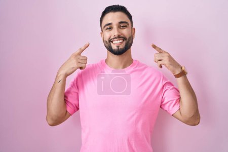 Téléchargez les photos : Jeune homme hispanique debout sur fond rose souriant pointant vers la tête avec les deux doigts de la main, bonne idée ou pensée, bonne mémoire - en image libre de droit
