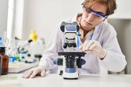 Téléchargez les photos : Jeune homme scientifique caucasien utilisant le microscope versant du liquide sur l'échantillon au laboratoire - en image libre de droit