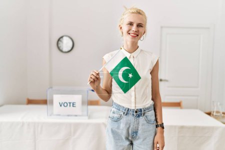 Photo for Young blonde woman holding pakistan flag smiling at electoral college - Royalty Free Image