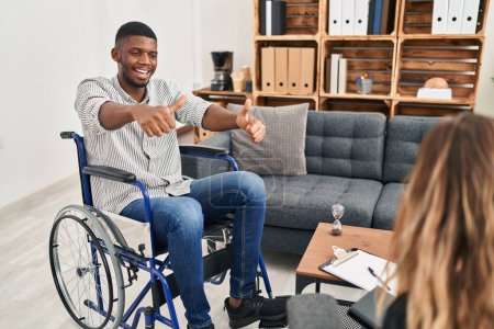 Photo for African american man doing therapy sitting on wheelchair approving doing positive gesture with hand, thumbs up smiling and happy for success. winner gesture. - Royalty Free Image